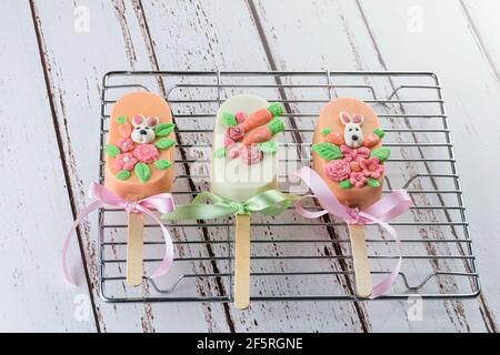 Karottenkuchencakesicles, verziert mit Kaninchen, Blumen und Schleife. Auf einem Metallgitter. Stockfoto