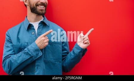 Glücklicher bärtiger Mann, der mit den Fingern auf den Kopierraum zeigt, isoliert auf rotem Hintergrund. Werbekonzept Stockfoto