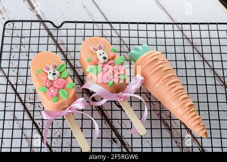 Karottenkuchencakesicles, verziert mit Kaninchen und Blumen. Neben einer weißen Schokoladenkarotte, einem Pint essbarer Orangenfarbe, gefüllt mit brigadeiro (br Stockfoto