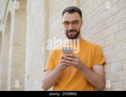 Schöner lächelnder Mann mit Handy, Kommunikation online, Video ansehen. Junge bärtige Hipster hält Smartphone-Shopping online Stockfoto