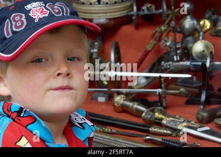 Kleiner Junge mit Hutfenstern in Rothenburg ob der Tauber und fasziniert sich von der Handwerkskunst des mittelalterlichen Waffenladens. Stockfoto