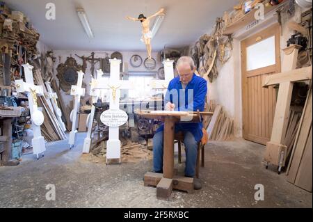 26. März 2021, Sachsen, Neudörfel: Nikolaus Dürlich schreibt in seiner Werkstatt mit einem Pinsel einen Namen auf eine Holzplatte. Der sorbische Holzbildhauer ist die dritte Generation, die Kreuze und religiöse Figuren herstellt und restauriert. Foto: Sebastian Kahnert/dpa-Zentralbild/dpa Stockfoto