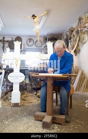 26. März 2021, Sachsen, Neudörfel: Nikolaus Dürlich schreibt in seiner Werkstatt mit einem Pinsel einen Namen auf eine Holzplatte. Der sorbische Holzbildhauer ist die dritte Generation, die Kreuze und religiöse Figuren herstellt und restauriert. Foto: Sebastian Kahnert/dpa-Zentralbild/dpa Stockfoto