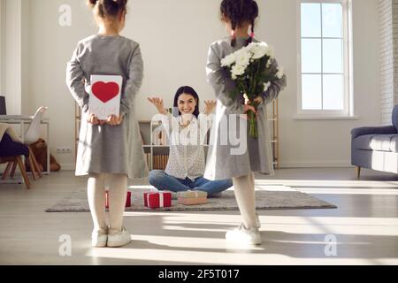 Zwei Töchter stehen mit dem Rücken zur Kamera und halten Blumen und eine handgemachte Postkarte. Stockfoto