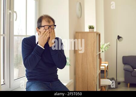 Porträt eines reifen Mannes mit Brillen reiben Augen sitzen auf Fensterbank Stockfoto