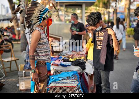 Nordamerikanisches Indianerkostüm, das von einem Straßenhändler getragen wird, während der Kunde ein T-Shirt kauft. Thailand Street Festival Südostasien Stockfoto