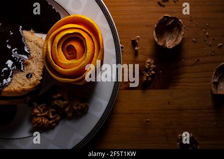 Walnusskuchen mit Orangenschale von Schokoladensauce auf dem Teller bei schwachem Licht. Stockfoto