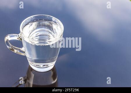 Noch sauberes Trinkwasser in transparentem Glas auf Oberfläche reflektiert Gegen blauen Himmel und Wolke Stockfoto