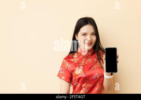 Chinesisch teen Mädchen zeigt Smartphone leeren Bildschirm Dressing Qipao traditionellen Tuch. Stockfoto