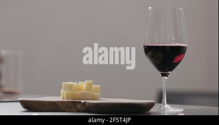 Rotwein in Weinglas mit Jahrgangskäse auf Olivenbrett, breites Foto Stockfoto