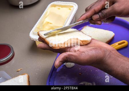 Nahaufnahme der Hände Auftragen von Butter auf Weißbrot mit Buttermesser Stockfoto