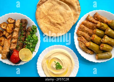 Gegrilltes Hähnchen, Kofta Kebab, Mahshi, Kohlbrötchen, Pita-Brot, Tahini auf weißem Teller auf blauem Hintergrund, Draufsicht. Kafta Kebab und Mahshi Stockfoto