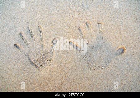 Handabdrücke auf dem Sand des Strandes mit Meereswellen. Draufsicht. Die Hände von zwei Personen markieren den Sand. Stockfoto