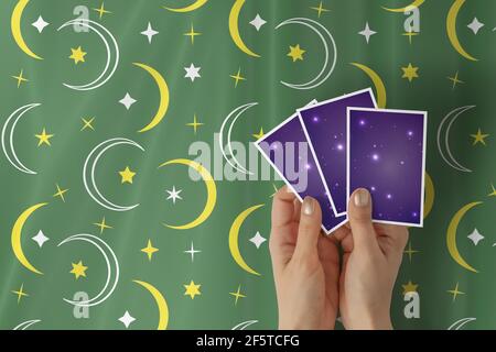 Hände einer jungen Frau mit goldenem Nagellack, der drei Tarot- oder oracle-Karten auf einem grünen Stern und einem Tischtuch mit Sichelmuster hält. Stockfoto