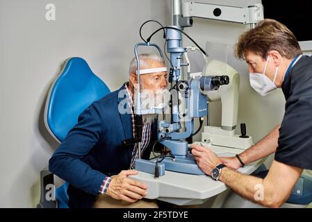 Seitenansicht des professionellen Augenarztes mit Spaltlampe und Kontrolle Sehvermögen des älteren männlichen Patienten Stockfoto