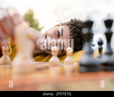 Von unten der optimistischen afroamerikanischen Frau, die am Tisch sitzt Im Park und Schach spielen, während Sie die Kamera betrachten Stockfoto