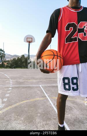 Cropped unkenntlich afroamerikanischen männlichen Streetball-Spieler in Uniform stehen Mit Ball auf dem Basketballplatz Stockfoto