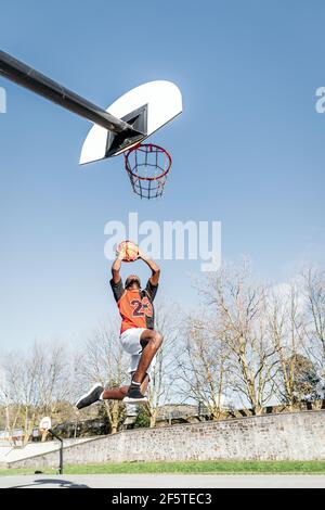Von unten von afroamerikanischen männlichen Streetball-Spieler im Moment Von Springen und Scoring Basketball im Reifen Stockfoto