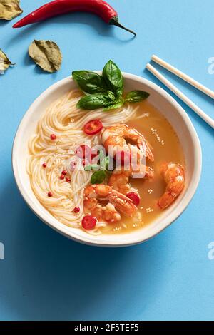 Tom Yum Suppe in Schüssel mit Essstäbchen auf blauem Hintergrund Stockfoto