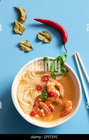 Tom Yum Suppe in Schüssel mit Essstäbchen auf blauem Hintergrund Stockfoto