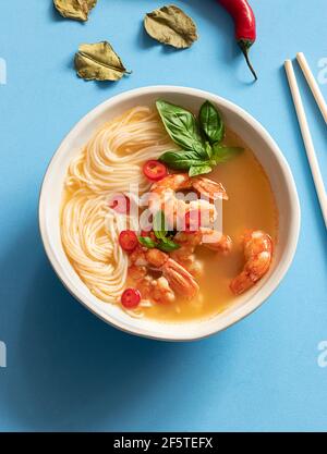 Tom Yum Suppe in Schüssel mit Essstäbchen auf blauem Hintergrund Stockfoto