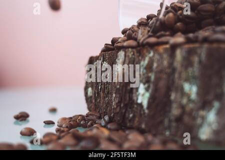 Kaffeebohnen, die aus einem Glasbehälter auslaufen, Nahaufnahme, Seitenansicht. Kaffeebohnen in einem Glas auf einem Holztablett. Kaffeebohnen Hintergrund. Stockfoto