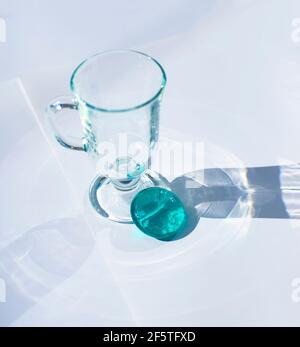 Glasbecher. Rundes türkisfarbenes Glas-Medaillon. Transparente gemusterte Schatten auf weißem Hintergrund.