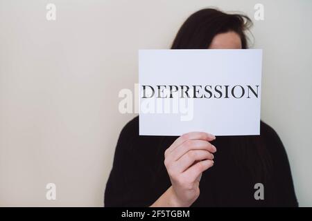 Frau mit weißem Papierbogen Karte mit Wort DEPRESSION isoliert auf beigem Hintergrund. Stockfoto