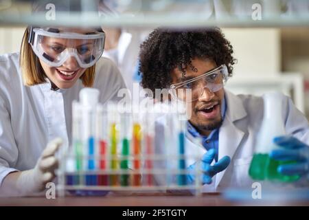 Junge Kollegen im Schutzkleidung beobachten chemische Reaktionen in einer Arbeitsatmosphäre im Universitätslabor. Wissenschaft, Chemie, Labor, Menschen Stockfoto