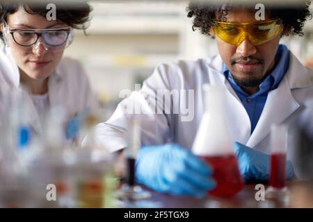 Junge Wissenschaftler beobachten in einer Schutzausrüstung chemische Reaktionen in der sterilen Laborumgebung. Wissenschaft, Chemie, Labor, Menschen Stockfoto