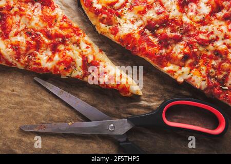 Scheiben frisch zubereiteter Pizza, in Dreiecke mit Küchenschere geschnitten, auf braunem Backpapier liegend Stockfoto