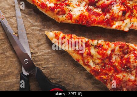 Scheiben frisch zubereiteter Pizza, in Dreiecke mit Küchenschere geschnitten, auf braunem Backpapier liegend Stockfoto