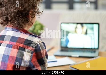 Online-Schulungen. Rückansicht des lateinischen Schuljungen Notizen machen, mit Online-Unterricht, mit Laptop während des Studiums zu Hause Stockfoto