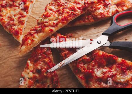 Scheiben frisch zubereiteter Pizza, in Dreiecke mit Küchenschere geschnitten, auf braunem Backpapier liegend Stockfoto