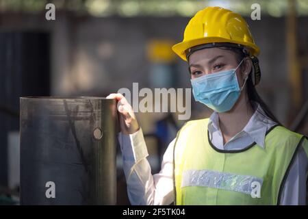 Ein Porträt einer Ingenieurin mit Maske, die in einer Fabrik steht. Arbeiten im Konzept der Produktionsanlage für die Schwerindustrie. Stockfoto