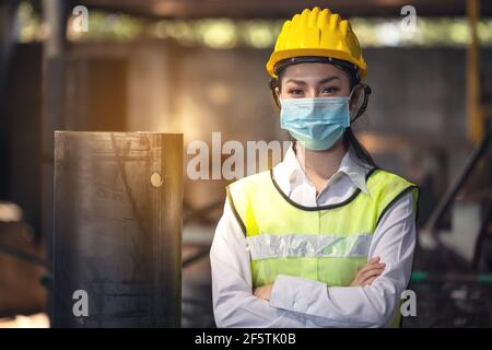 Ein Porträt einer Ingenieurin mit Maske, die in einer Fabrik steht. Arbeiten im Konzept der Produktionsanlage für die Schwerindustrie. Stockfoto