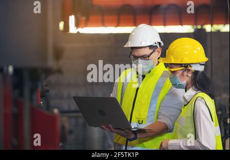 Zwei Techniker mit Schutzhelm und Laptop für die Planung eines Projekts. Vorarbeiter erklärt der Mitarbeiterin die Maschinen Stockfoto