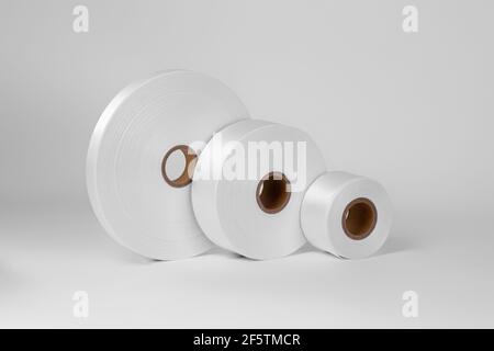 Seitenansicht ein Turm aus drei Spulen von weißen Satinbändern in verschiedenen Größen auf der Seite für Etiketten oder Branding, isoliert auf einem weißen, grauen Hintergrund Stockfoto