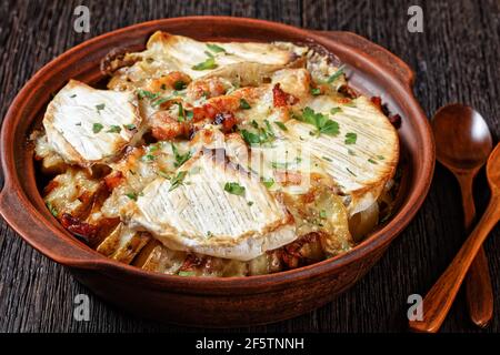 Tartiflette, French Potato, Bacon und Käse Auflauf in einer Tonschale auf einem dunklen Holztisch mit Löffeln, französische Küche Stockfoto
