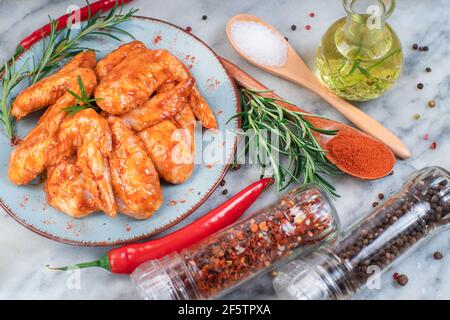 Marinierte Hähnchenflügel mit verschiedenen Gemüsesorten auf einer marmornen Küchenplatte.marinierte Hähnchenflügel auf einem Backblech mit Gemüse, Tomaten und TL Stockfoto