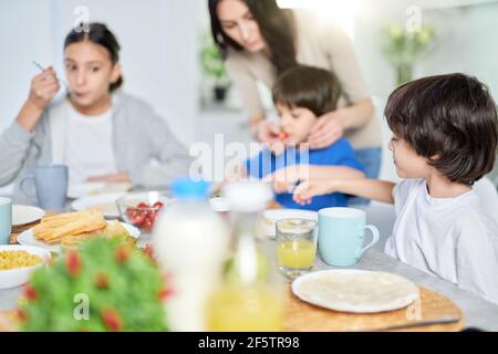 Nette kleine hispanische Junge mit Frühstück zusammen mit seiner Mutter und Geschwister. Lateinische Familie genießen zusammen Essen, sitzen am Küchentisch bei Stockfoto