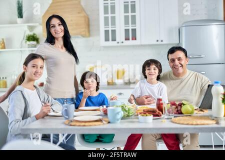 Gemeinsam essen. Lächelnde hispanische Eltern verbringen Zeit mit ihren kleinen Kindern und frühstücken zusammen zu Hause Stockfoto