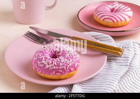 Zwei zuckerbeschichtete Donuts liegen auf einer rosa Keramikplatte. Stockfoto