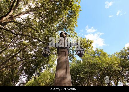 Weitwinkelansicht einer alten Steinlaterne an der historischen Königsallee in der Düsseldorfer Innenstadt, umgeben von grünen Bäumen. Stockfoto