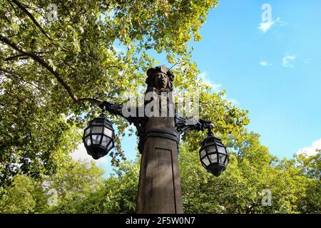 Alte Steinlaterne an der Einkaufsmeile Königsallee in der Düsseldorfer Innenstadt, umgeben von alten grünen Bäumen. Stockfoto