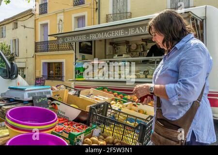 Frau, die an einem Obststand auf einem französischen Markt im Languedoc-Dorf St. Genies de Fontedit einkauft. Käsestall im Hintergrund. Stockfoto
