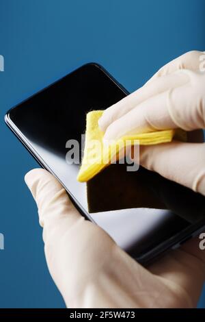 Reinigen des Handybildschirms mit einem gelben Tuch und Gummihandschuhen. Schmutziges Smartphone-Display mit Keimen. Weichfokus. Reinigungskonzept Stockfoto