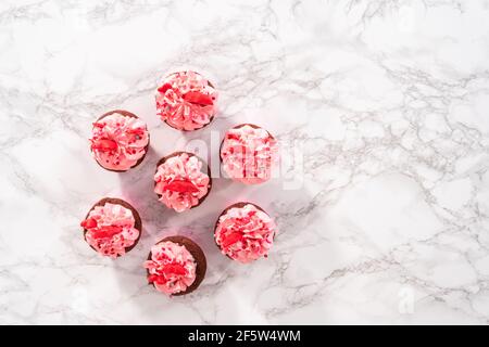 Flach liegend. Rote Samt Cupcakes mit rosa italienischen Buttercreme Zuckerguss und schmückt mit Herz und küssförmigen roten Pralinen. Stockfoto