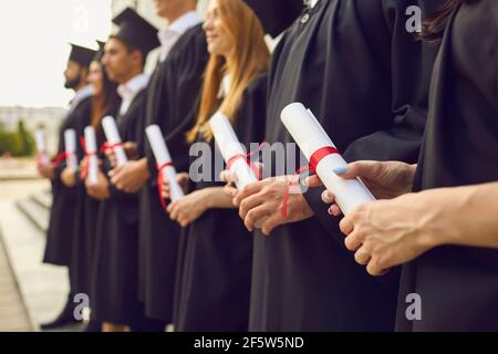 Graduate Concept.Cropped Bild der Reihe von Studenten in schwarzen Roben Mit Diplomen in den Händen bei der Abschlussfeier Stockfoto