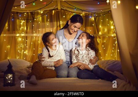 Portrait der Mutter umarmt zwei kleine Töchter im Zelt sitzen Zu Hause Stockfoto